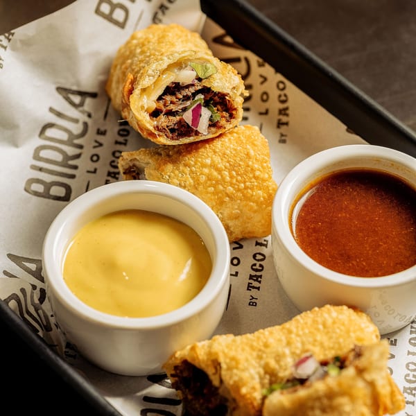Birria Love egg rolls with two dipping sauces on branded parchment paper.