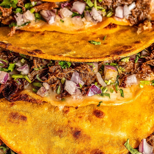 Close-up of Birria Love's birria tacos, filled with shredded meat, melted cheese, and diced onions.