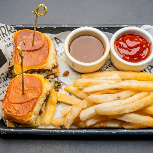 Birria Love sliders with fries, ketchup, and a dipping sauce on a black tray.