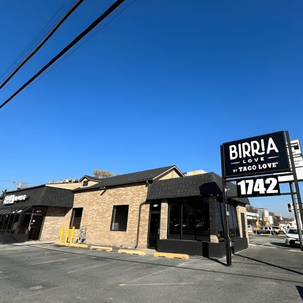 Exterior of Birria Love restaurant, a brick building with a large black sign under a clear blue sky.