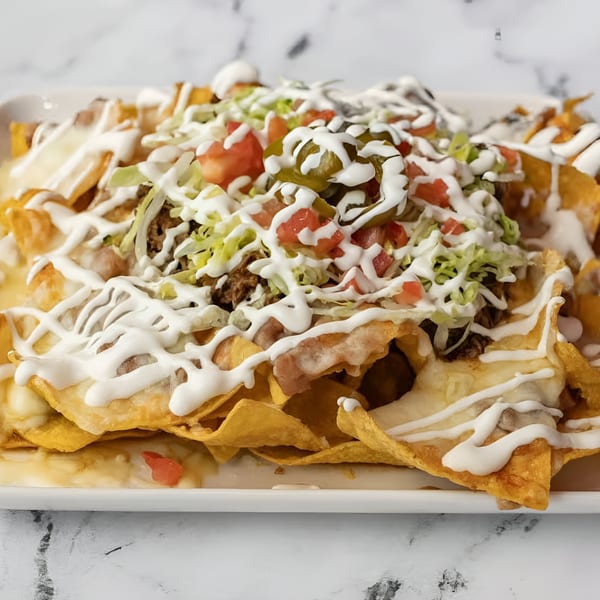 A large plate of Birria Love nachos, topped with meat, cheese, lettuce, tomatoes, jalapeños, and sour cream.