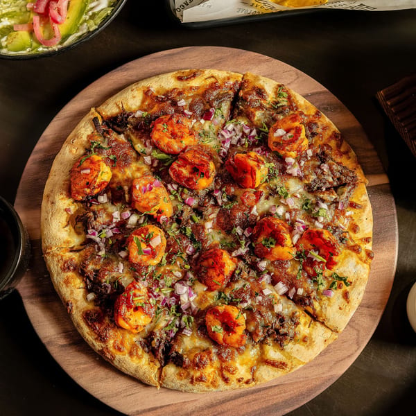 Birria Love's Mexican pizza, topped with shrimp, birria, red onions, and cilantro on a wooden board.