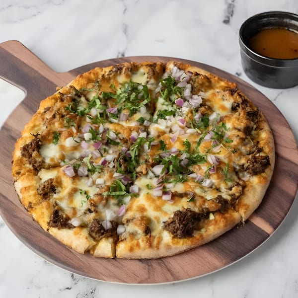 Birria Love's birria pizza, topped with shredded meat, cheese, red onions, and cilantro, with consommé.