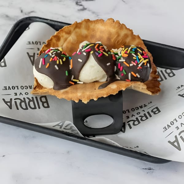 Three scoops of ice cream with chocolate and sprinkles in a waffle taco shell on a black tray.