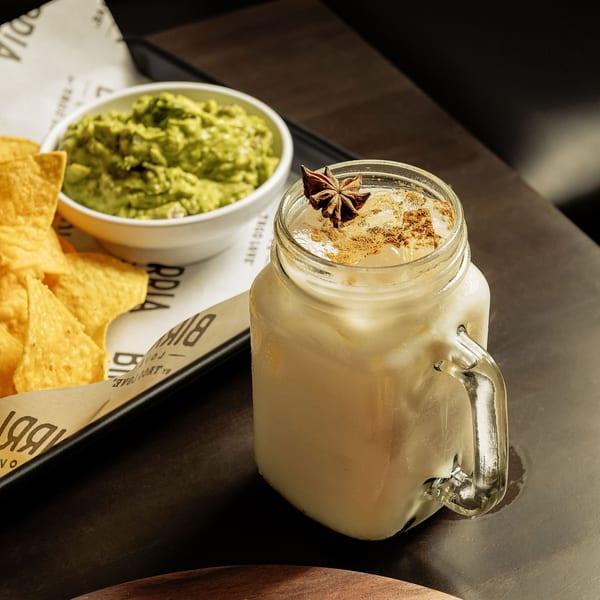 Horchata with star anise and cinnamon, alongside tortilla chips and guacamole on a dark table.