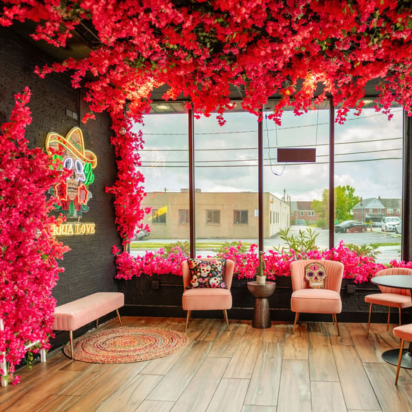 Birria Love restaurant interior with pink floral decor, neon skull sign, and plush seating.