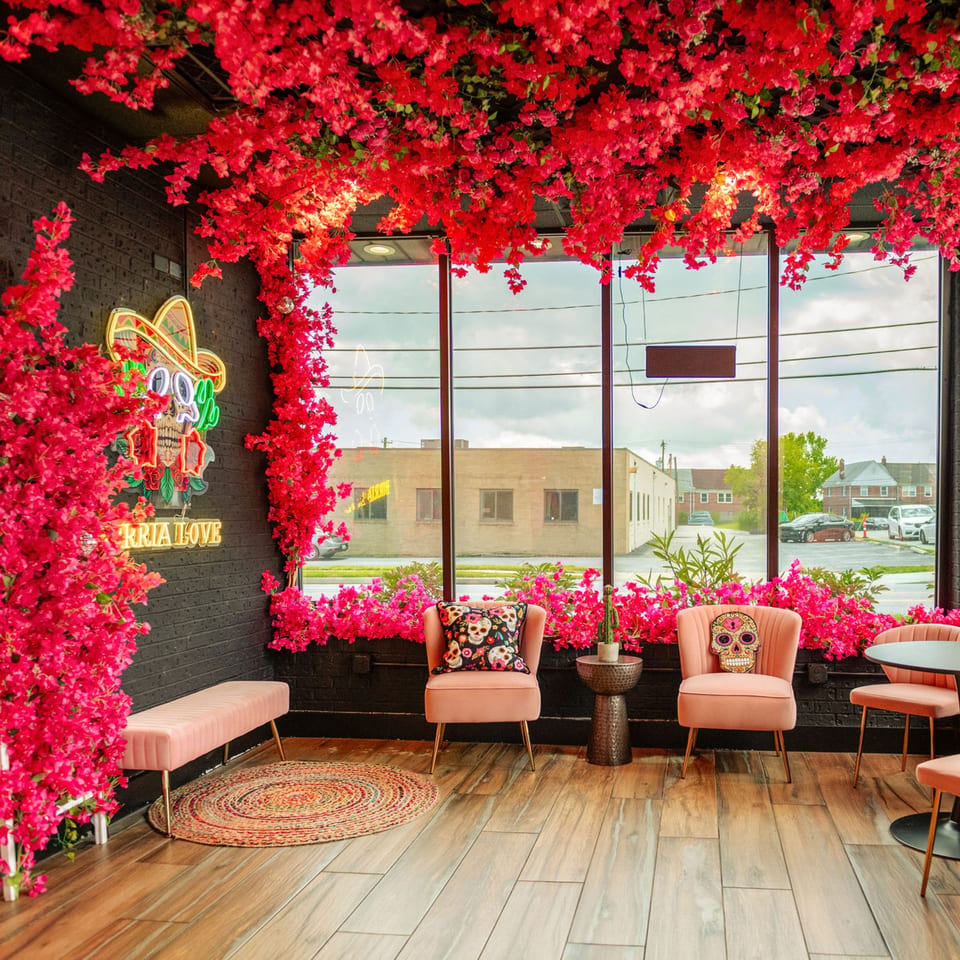 Birria Love restaurant interior with pink floral decor, neon skull sign, and plush seating.