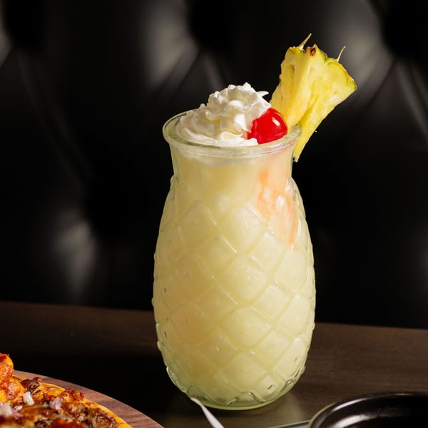 Pineapple-shaped glass filled with a frozen drink, topped with whipped cream, a cherry, and pineapple slice.